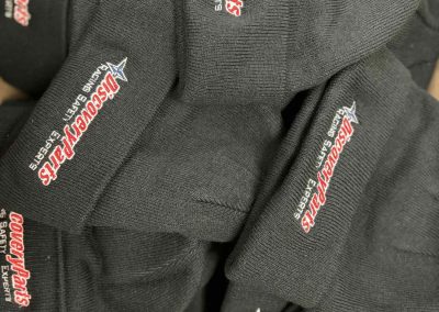 Stack of charcoal knit beanies with a red and white embroidered logo by 400 Ink