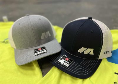 Gray and navy Richardson trucker hats with an embroidered tan logo by 400 Ink
